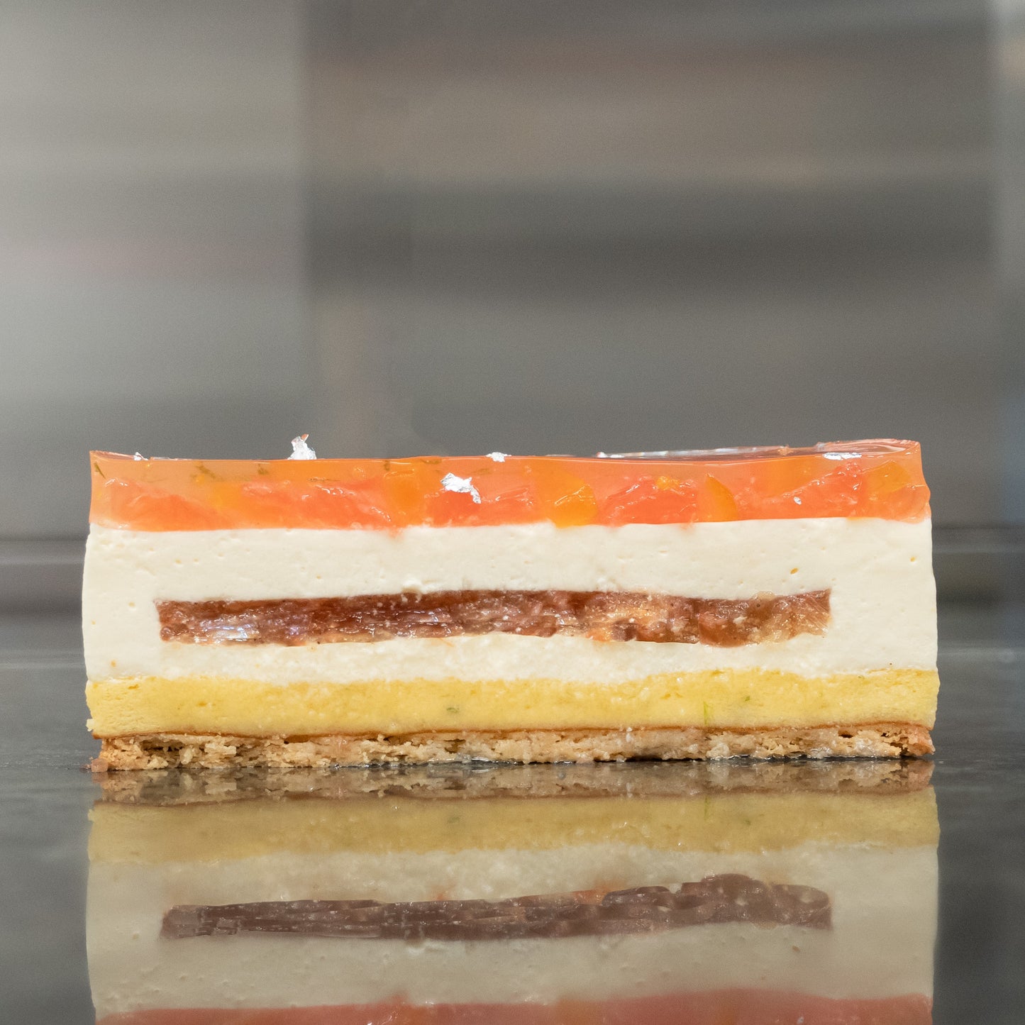 Layered cake with sablé Breton and lime sponge on the bottom, fromage blanc mousse in the middle, and grapefruit Timur pepper confit on top Topped with a jelly layer of grapefruit and confit kumquat A delicious treat for any occasion or special indulgence Cross-section view showcasing the different layers and textures of the cake